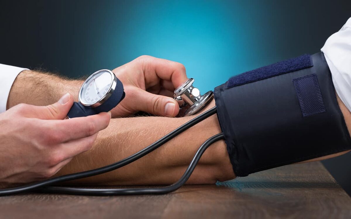 Blutdruckmessung am Arm eines Patienten mit Manometer und Stethoskop.