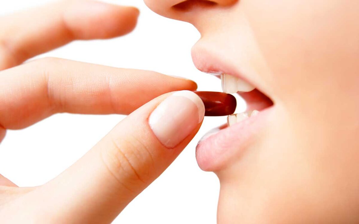 Eine Person nimmt eine rote Kapsel ein, Nahaufnahme der Hand und Lippen.