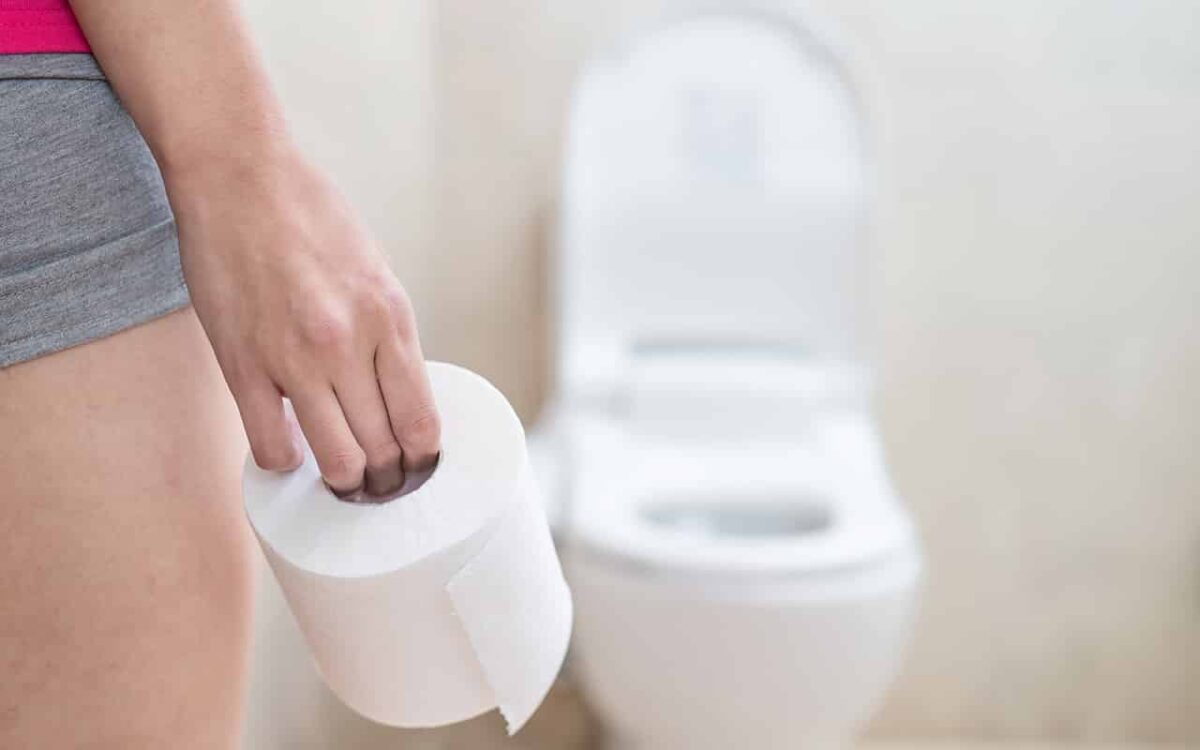 Person hält Toilettenpapier neben einer Toilette. Badezimmer Hygiene.