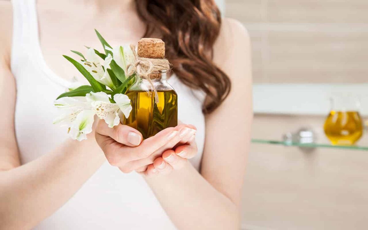 Frau hält Glasflasche mit ätherischem Öl und Blumen in Händen. Entspannte Wellness-Atmosphäre.