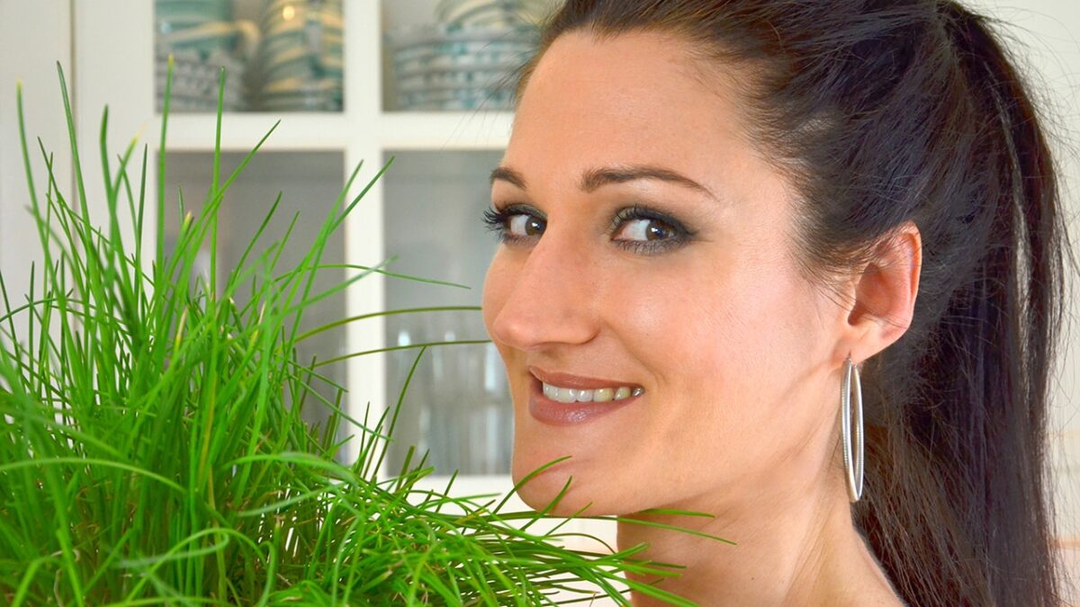 Frau lächelt neben einem Topf mit frischem Schnittlauch in einer modernen Küche.