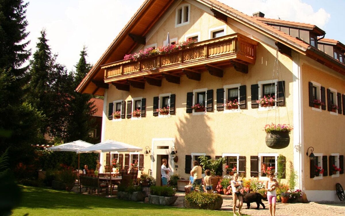 Traditionelles bayerisches Haus mit Balkon, Garten und spielenden Kindern im Sommer.