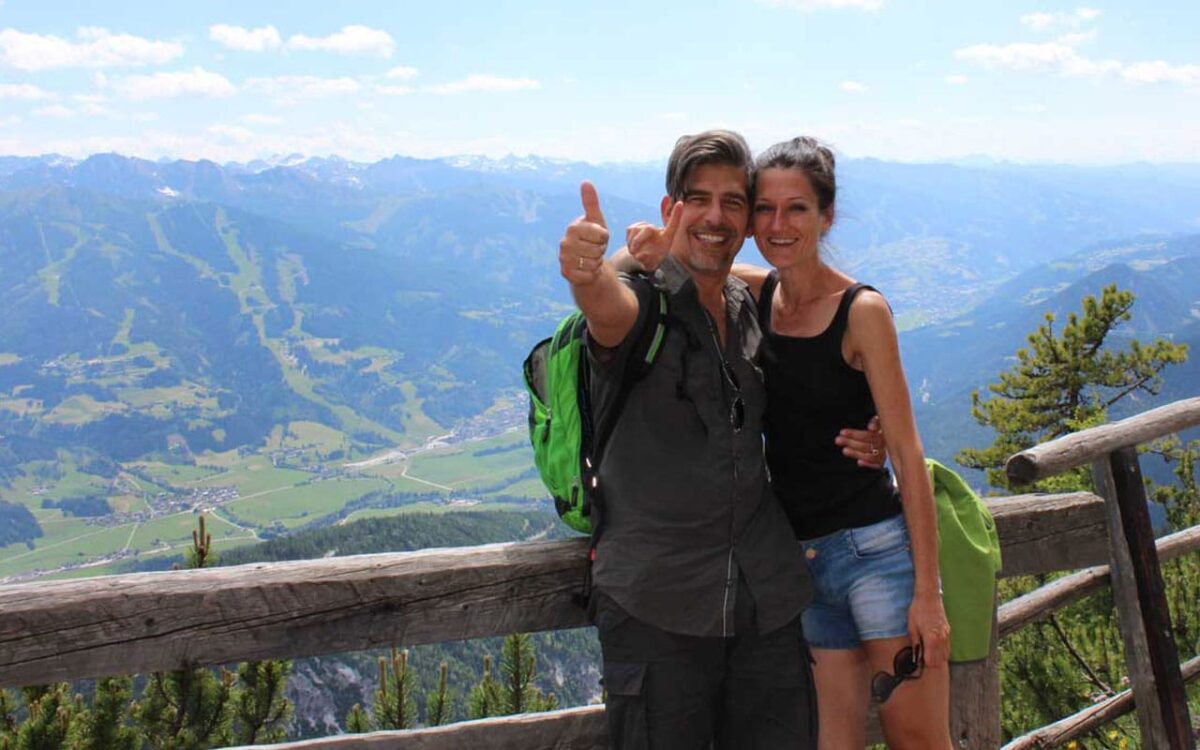 Paar beim Wandern auf Berggipfel mit atemberaubender Aussicht, sonniges Wetter.