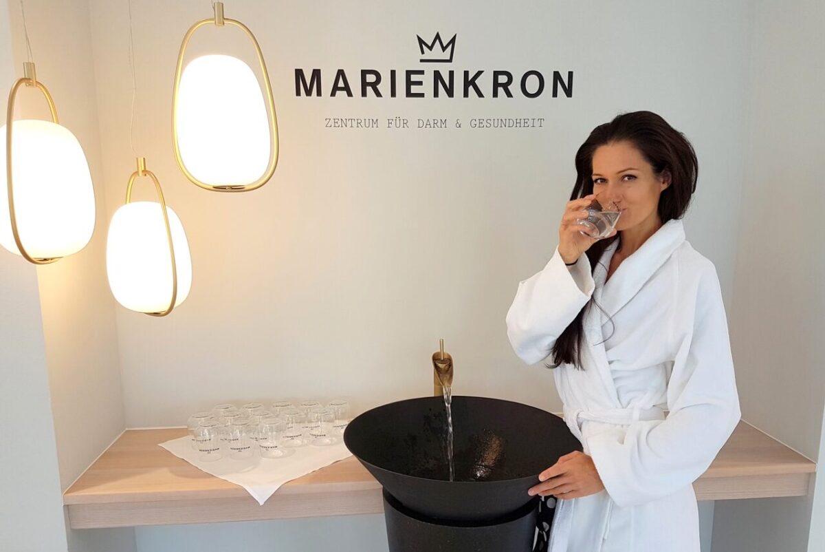 Frau in weißem Bademantel trinkt Wasser bei Marienkron Kurzentrum, gesundheitsförderndes Ambiente.